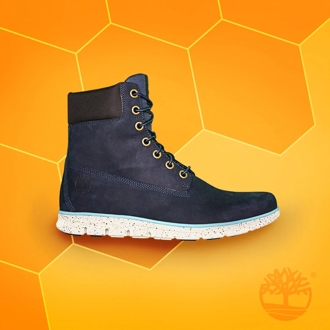 Black Timberland-style boot with a speckled white sole, set against an orange background with hexagonal patterns.