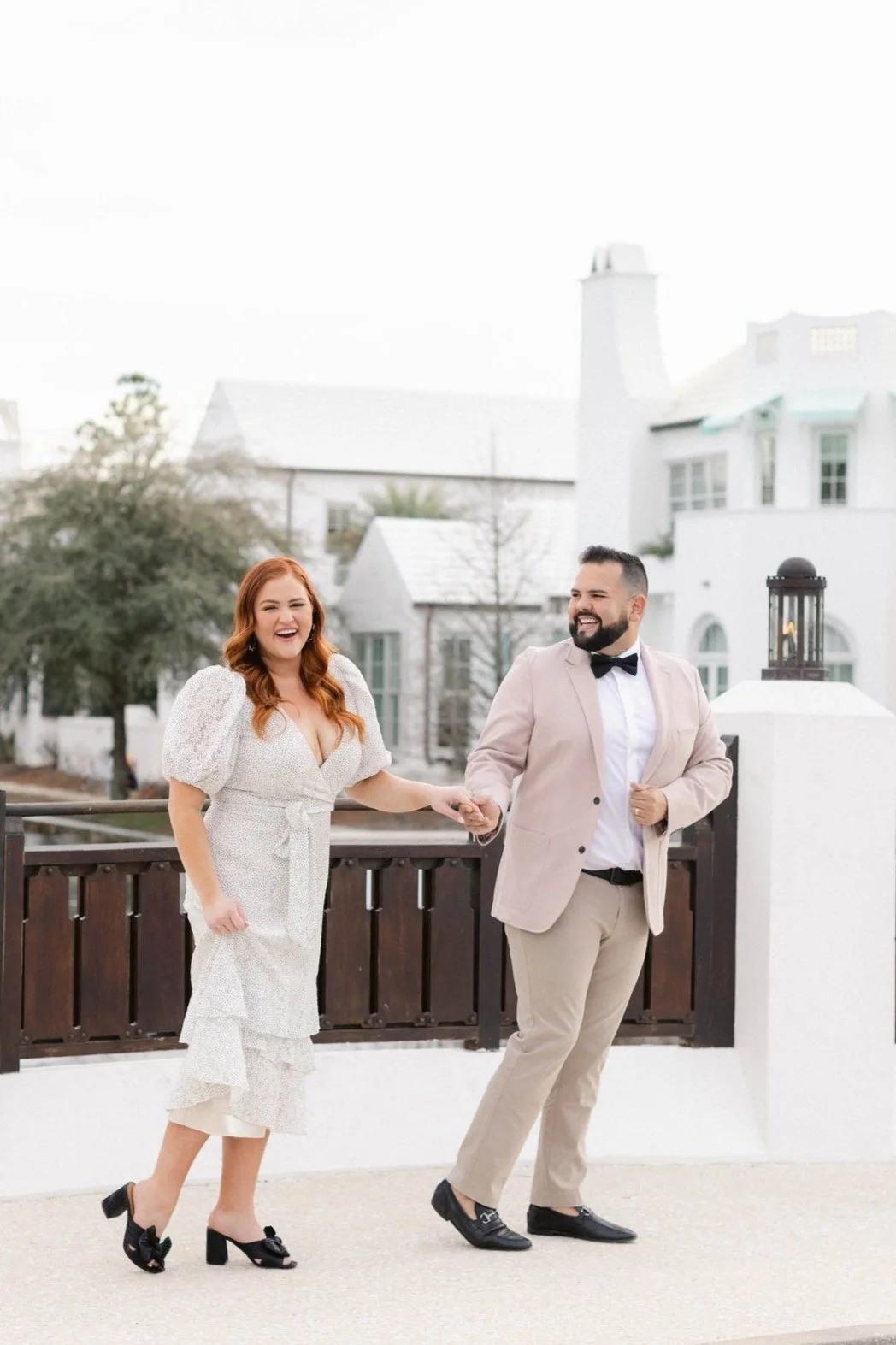 Photo of Autumn & Jendry walking together holding hands with white buildings in the background