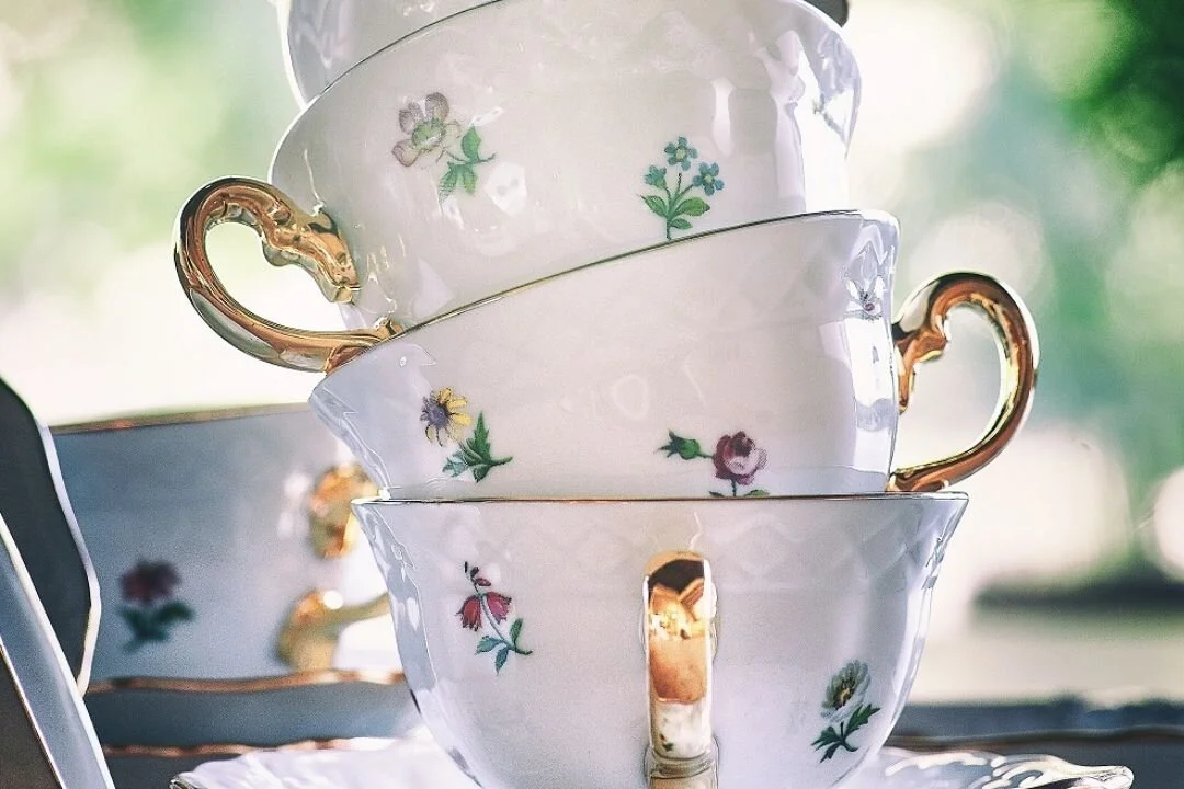 4 white china tea cups with floral print and golden handles stacked inside each other.
