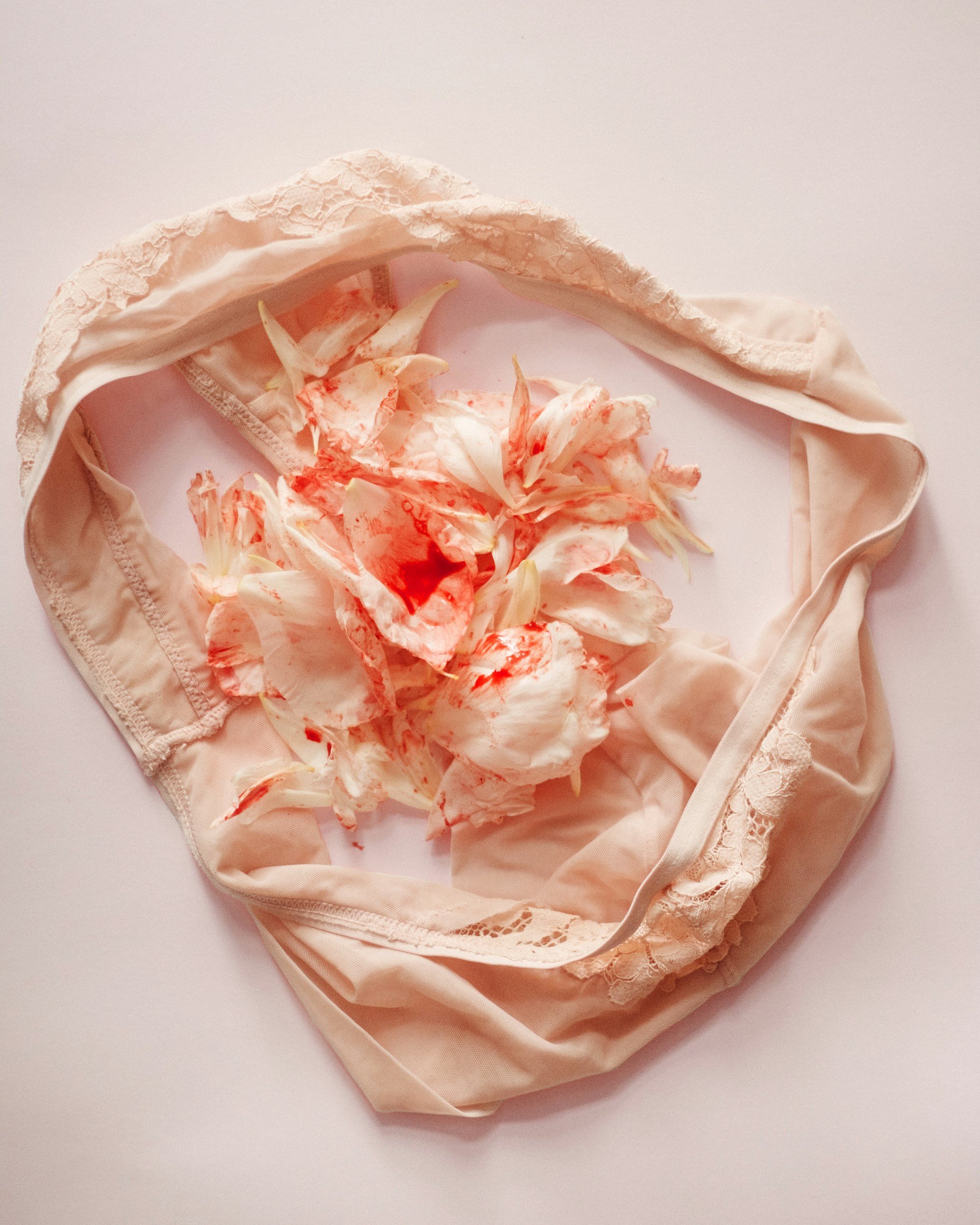 A pair of beige women's underwear with lace trim, stained with white and red substances resembling perfume or makeup, and red liquid.