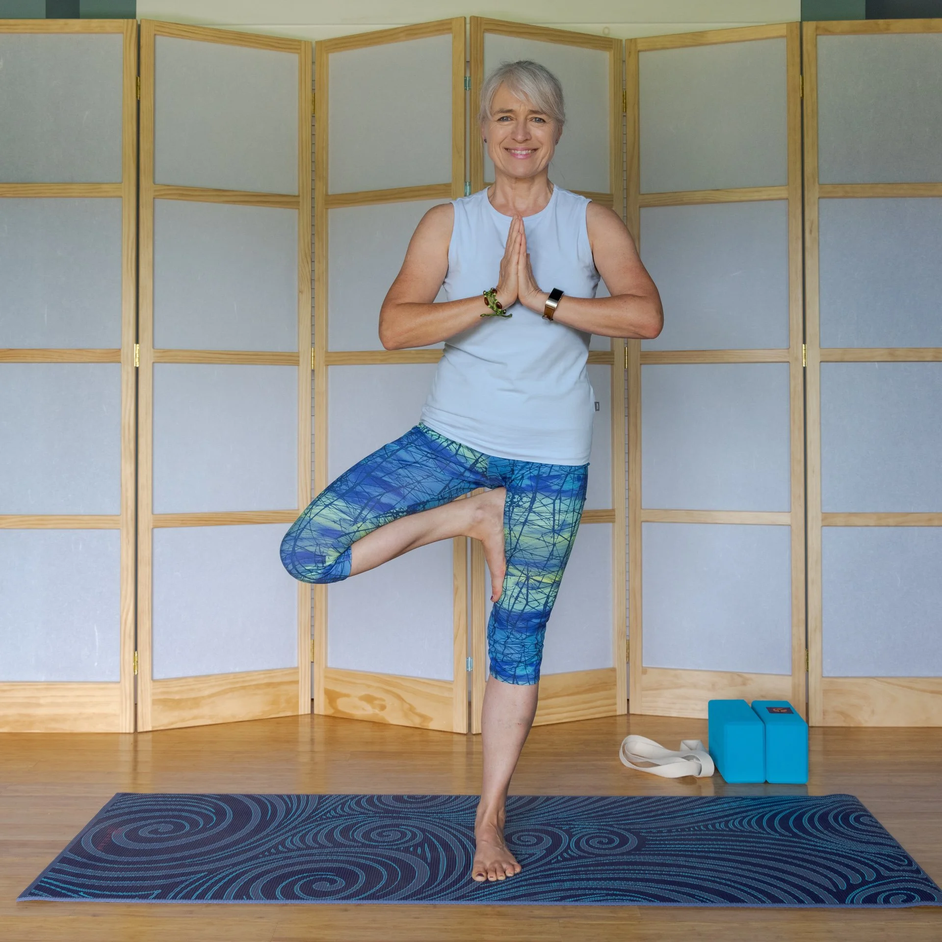 Doris Bittruff of happycat.yoga standing on a yoga mat, balancing on one leg with her other foot resting on her inner thigh, and her hands pressed together in a prayer-like position.
