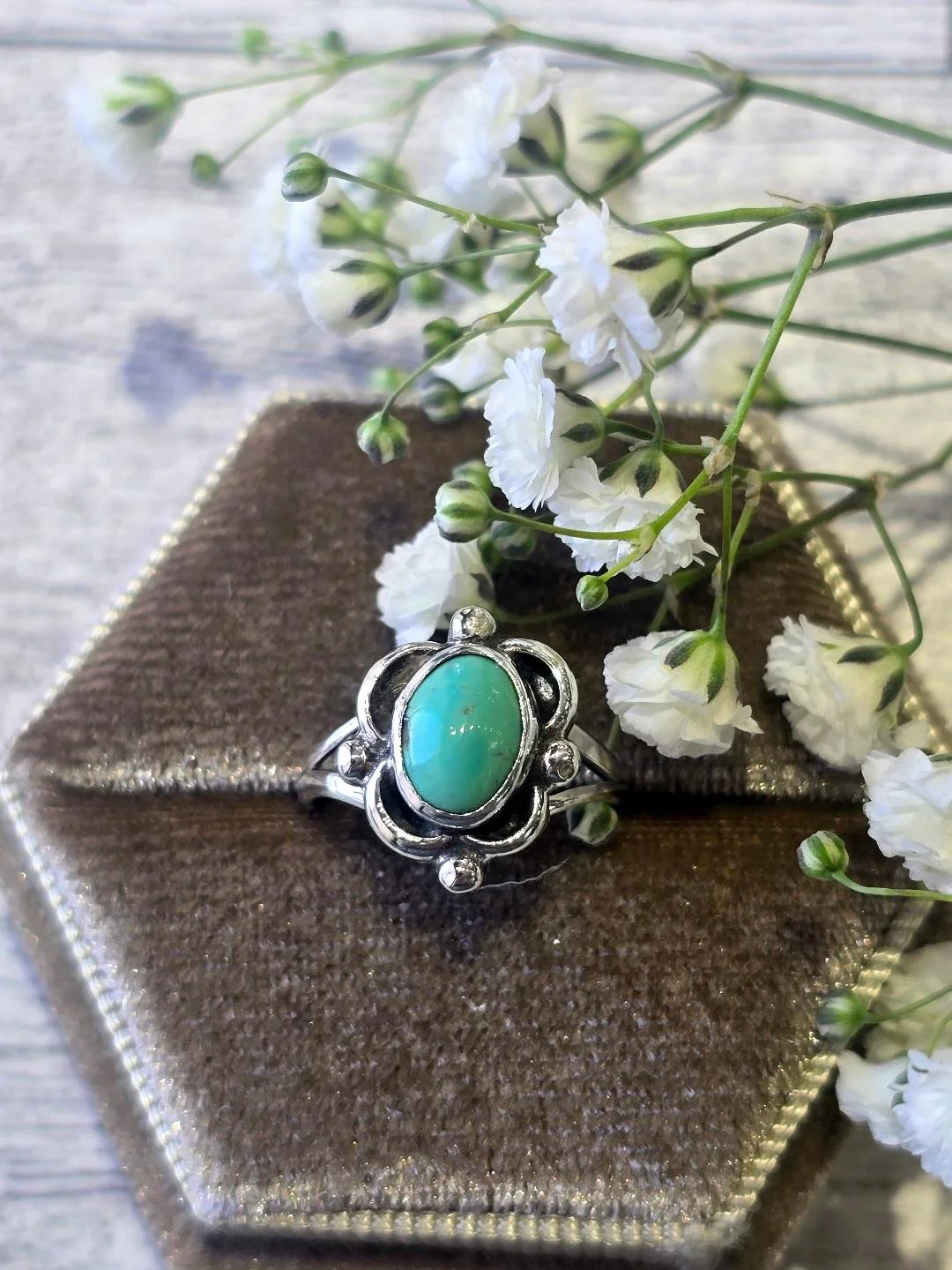 Front view of oval turquoise ring in a brown box with small white flowers
