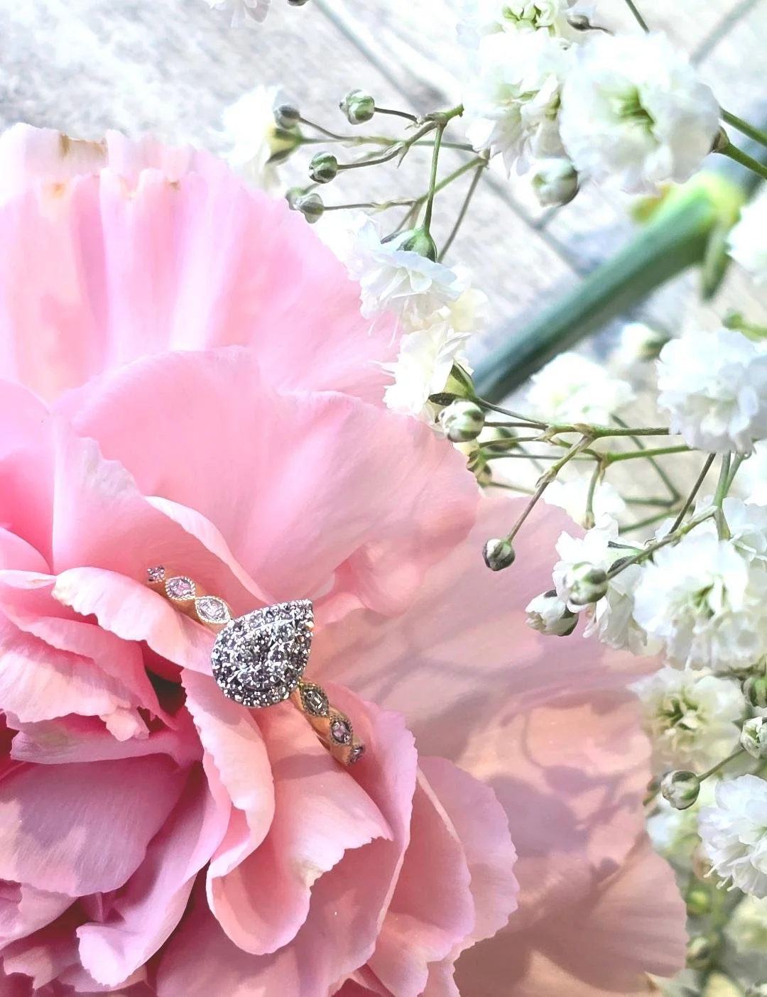 Angled view of yellow gold pear shaped ring set in a pink carnation with white flower