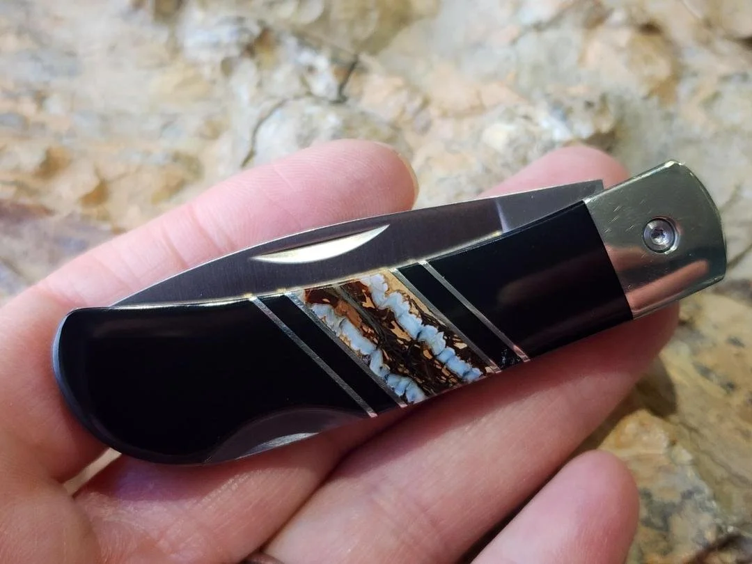 hand holding 3" knife with mammoth tooth inlay and onyx with rock in background
