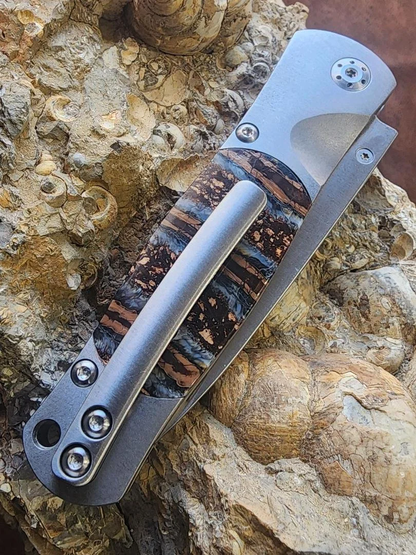 back of knife with clip with mammoth tooth handle on rock