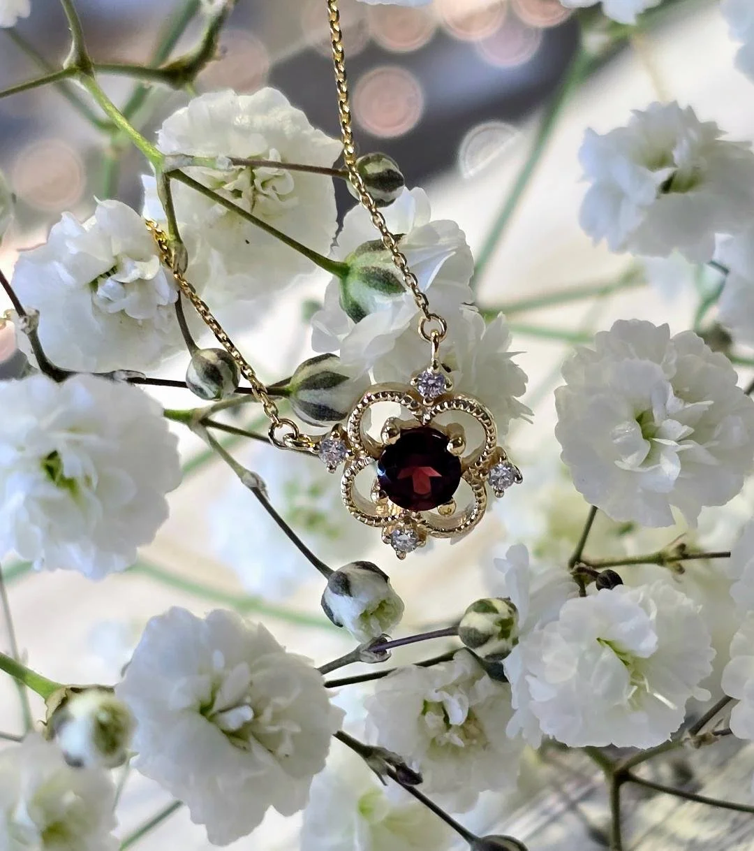 Angled view of yellow gold garnet pendant on a small white flower background