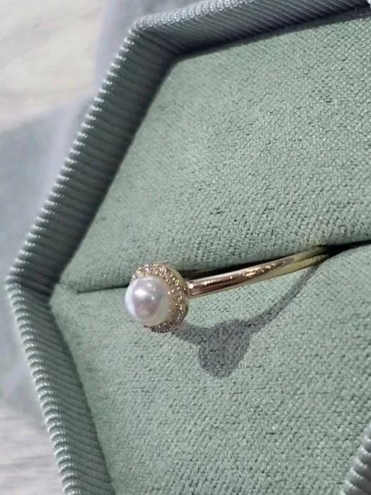yellow gold ring with freshwater cultured pearl and halo of round diamonds in a green box with a wood back round