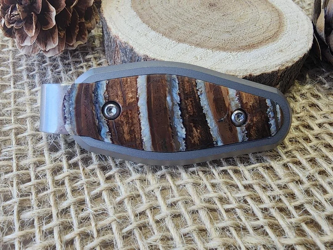 money clip inlayed with mammoth tooth on burlap with wood slice and pinecones in background