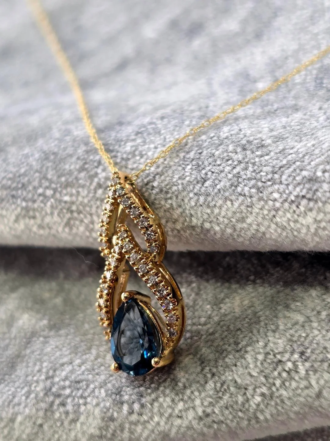 Side view of a yellow gold London blue topaz pendant set of a grey velvet background