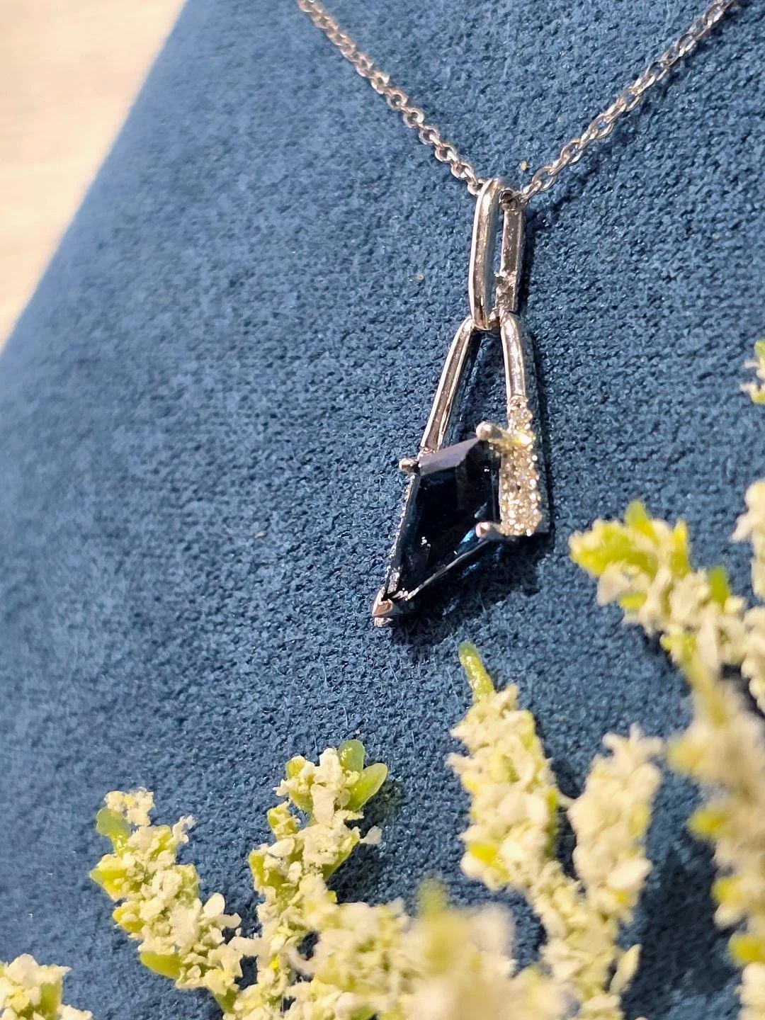 Side view of white gold London blue topaz necklace in a navy blue box on a white wooden background