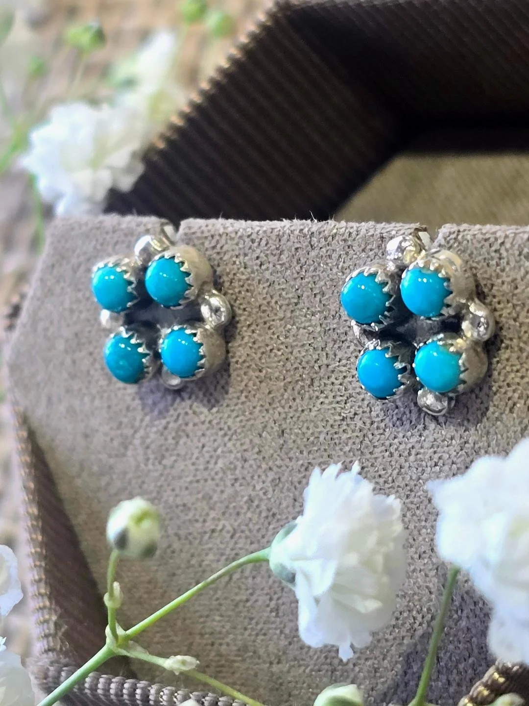 Side view of silver turquoise studs in a brown bracelet with small white flower set on top