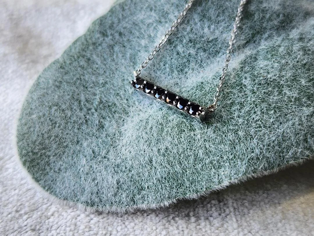 white gold black diamond bar necklace on leaf on grey fabric in background