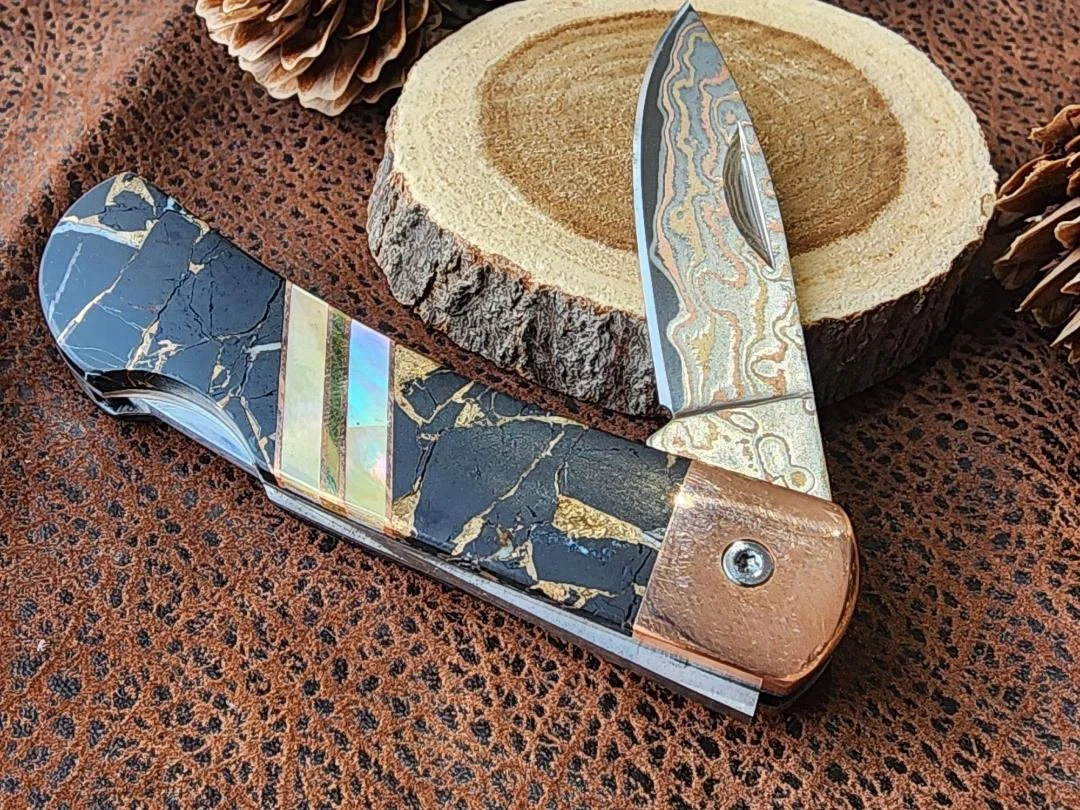 black buffalon inlay with mother of pearl accents on folding damascus pocketknife with pinecone and wood in back ground