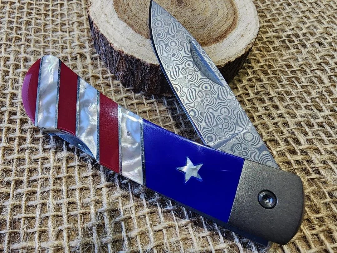 open 3" knife with raindrop Damascus blade with a patriotic inlay on handle with burlap and wood back ground