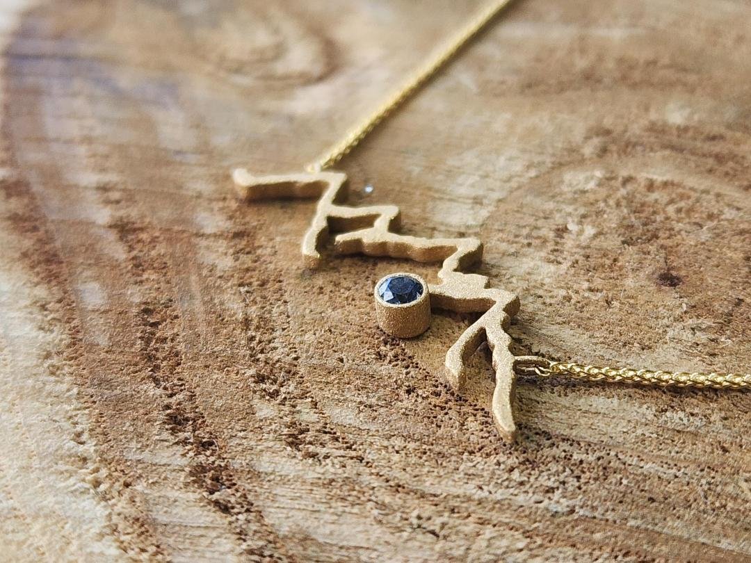 side view Yellow gold mountain range necklace with round blue sapphire on wood slice
