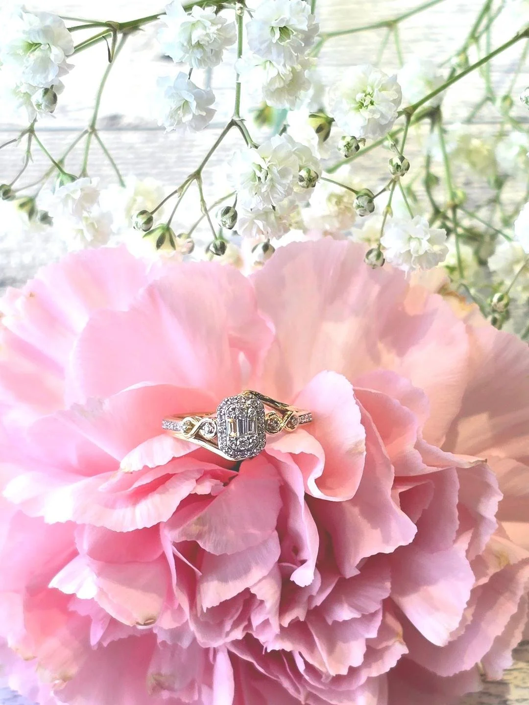Front view of a yellow gold engagement ring set in a pink carnation with small white flowers