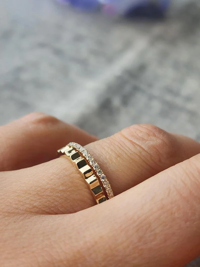Yellow gold Textured band style ring with round diamonds on women's hand with grey fabric with flowers in background