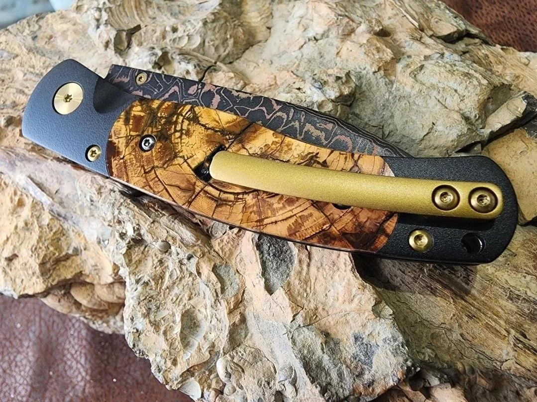 copper and brass back clip of Damascus knife with Mammoth ivory inlay on rock