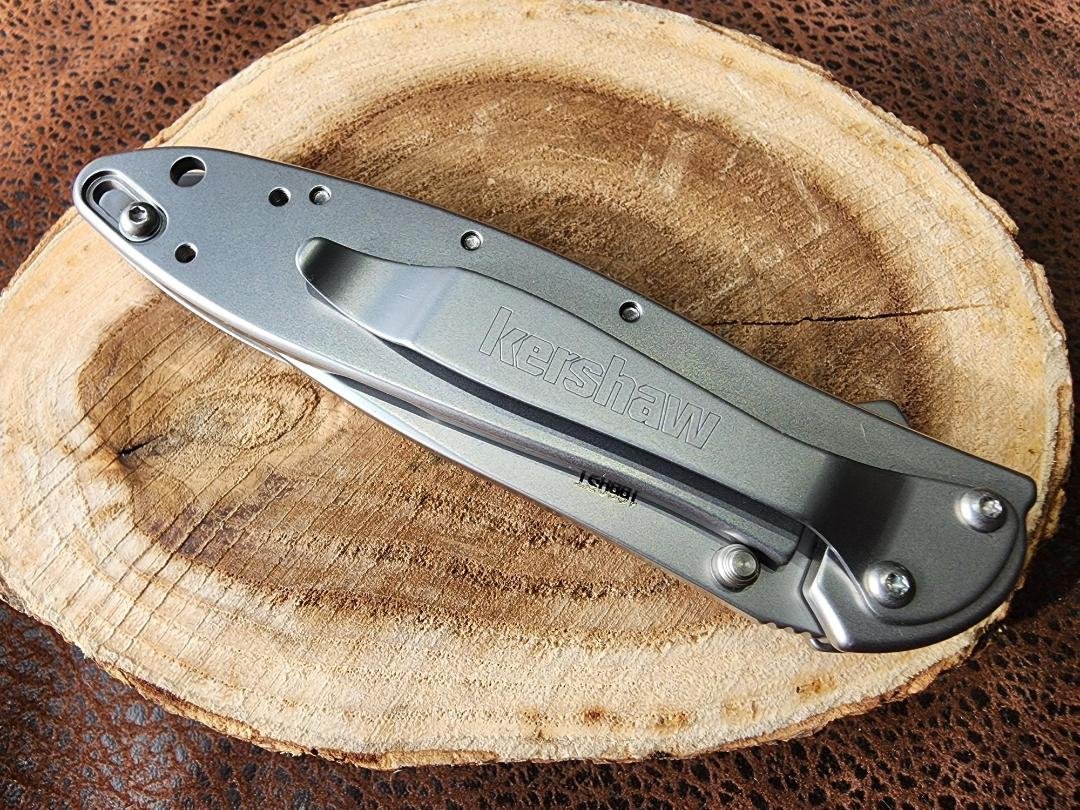 back of closed knife with a agatized dinosaur inlay on handle on wood slice and imitation leather background