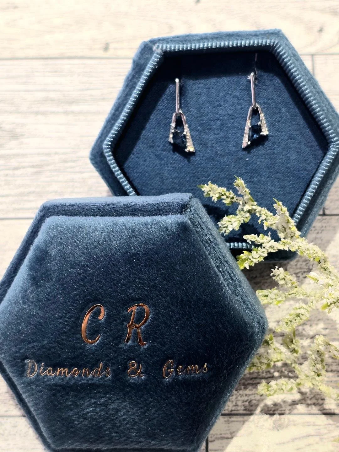 Front view of white gold London blue topaz earrings in a navy blue box with a white wooden background