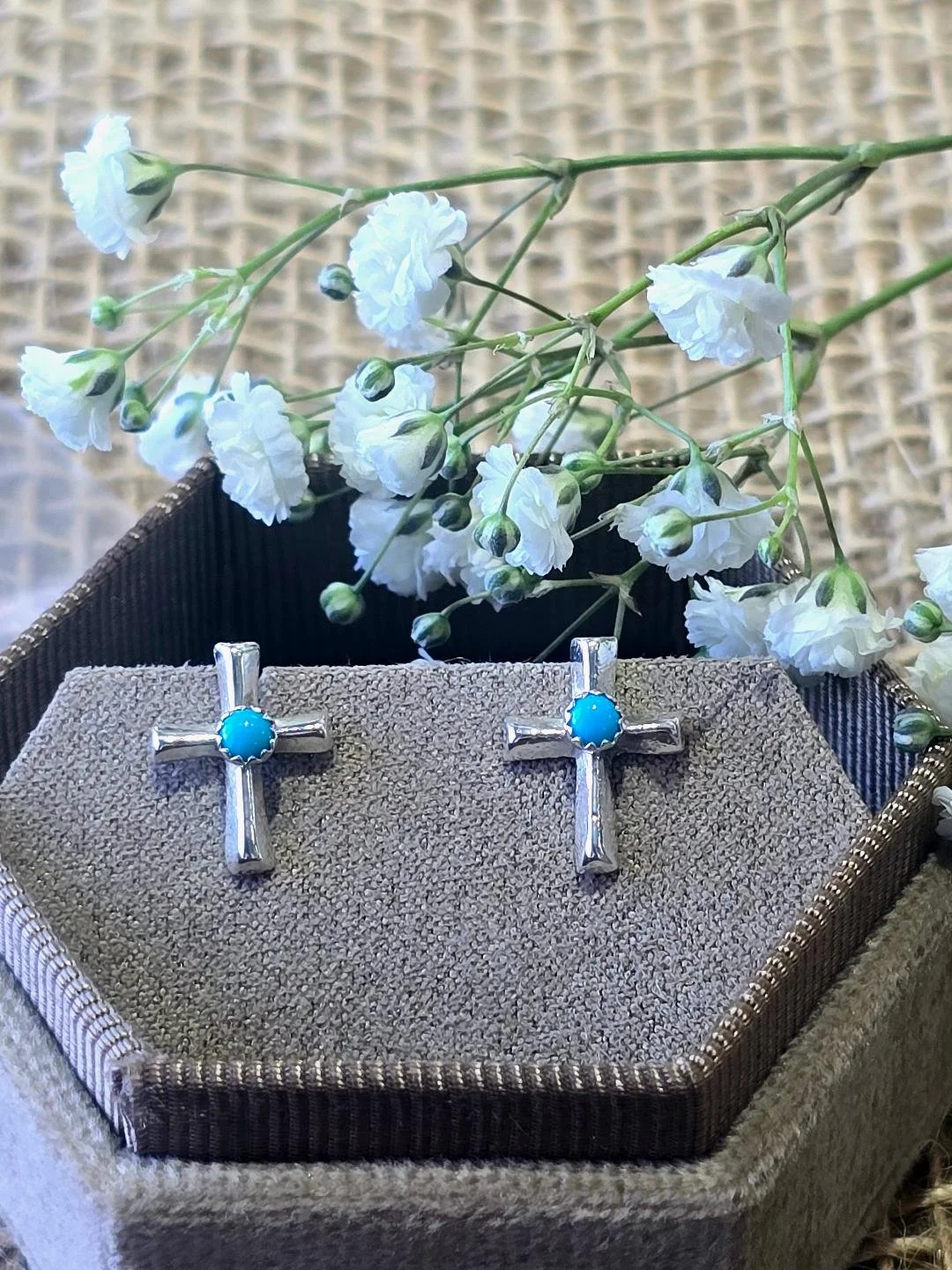 Front view of silver polished cross studs in a brown box with small white flowers set on top