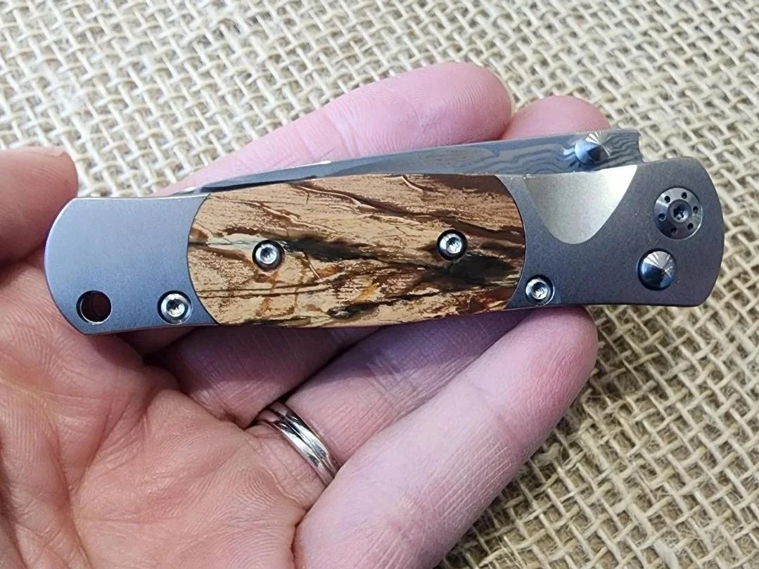 hand holding damascus folding pocket knife with button lock and mammoth tusk ivory on burlap background