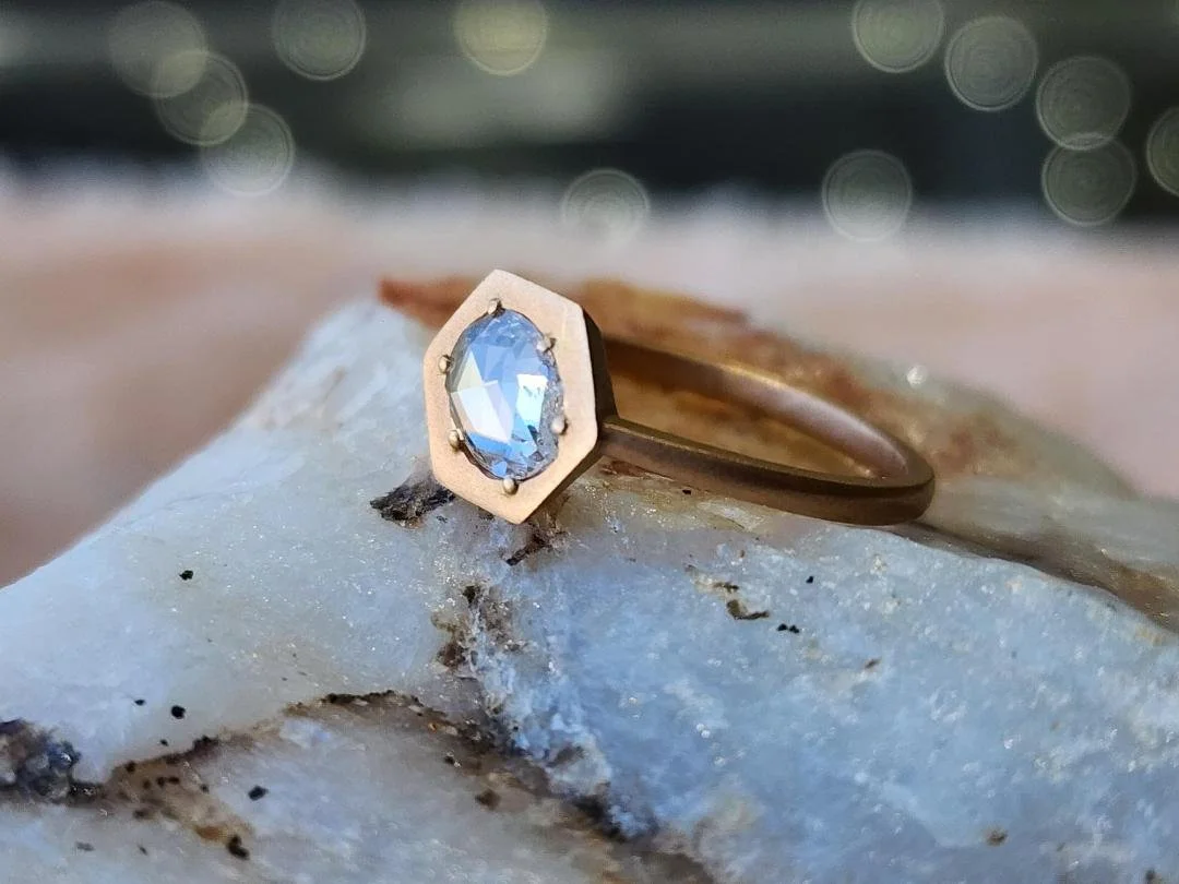 Brushed Rose gold diamond ring with rose cut diamond  resting on white quartz with pink and black background