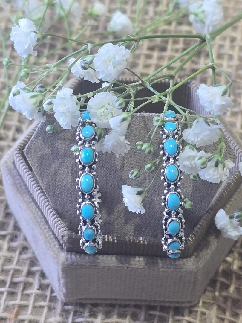 Front view of oval turquoise hoops in brown box with white flowers