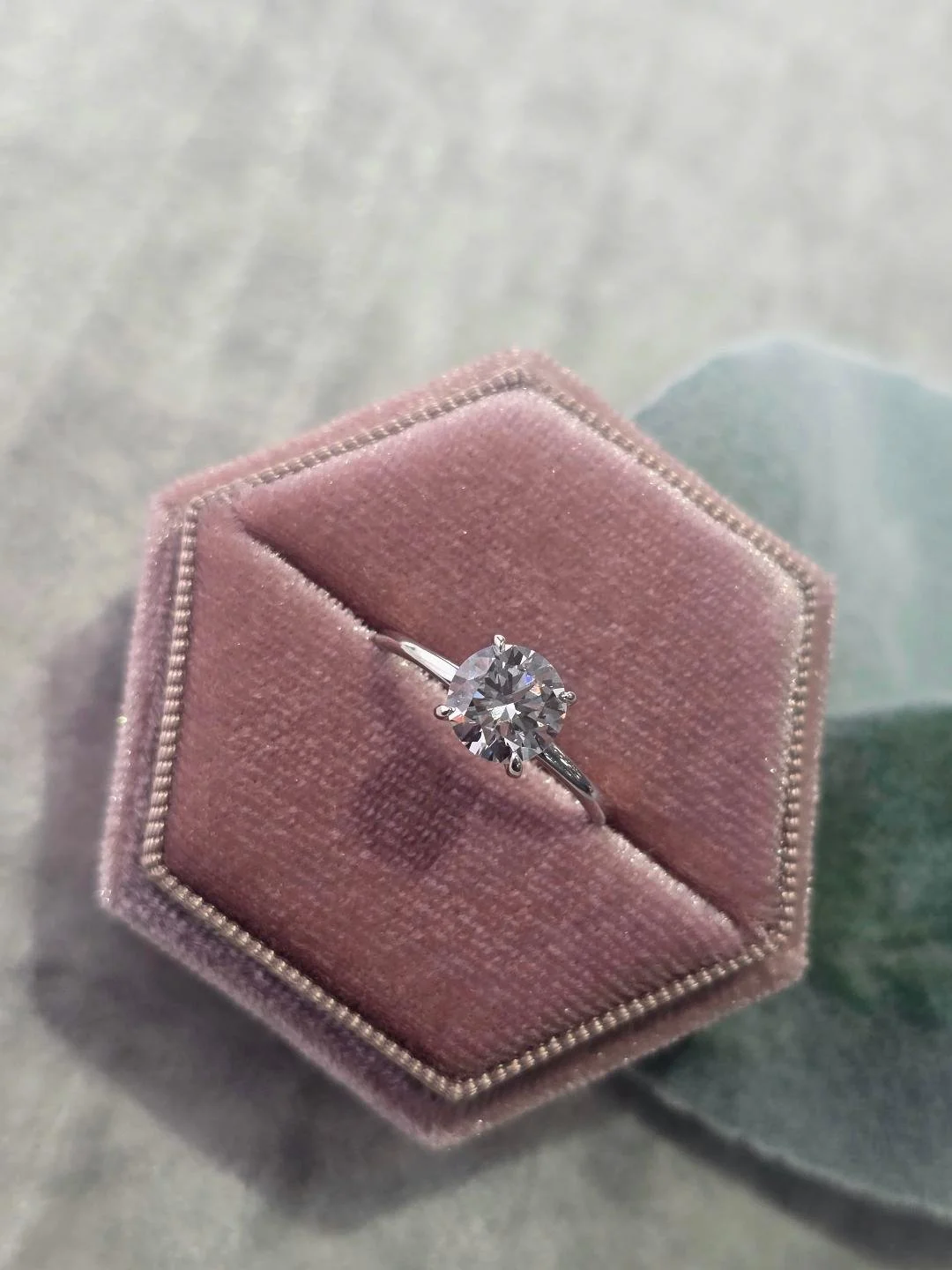 Angled front view of white gold lab grown solitaire set in a pink velvet box with leaf's in the background
