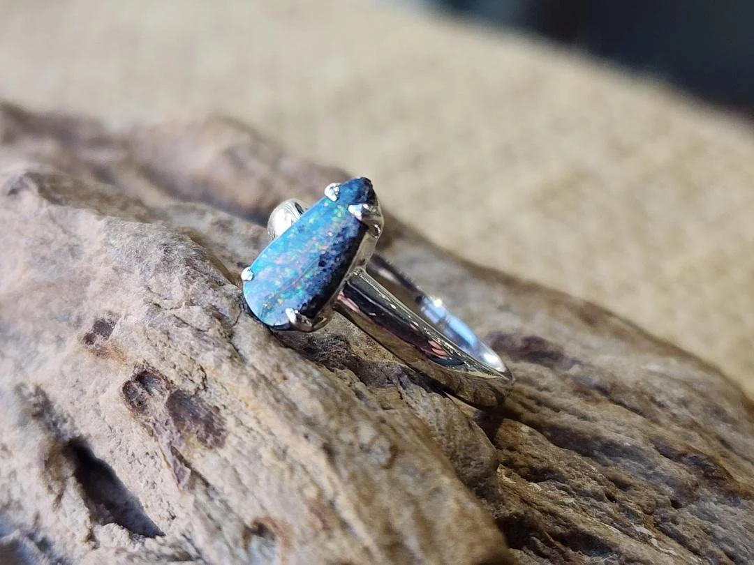 side view free form boulder opal set in a sterling silver ring set on a rock with burlap in the background.