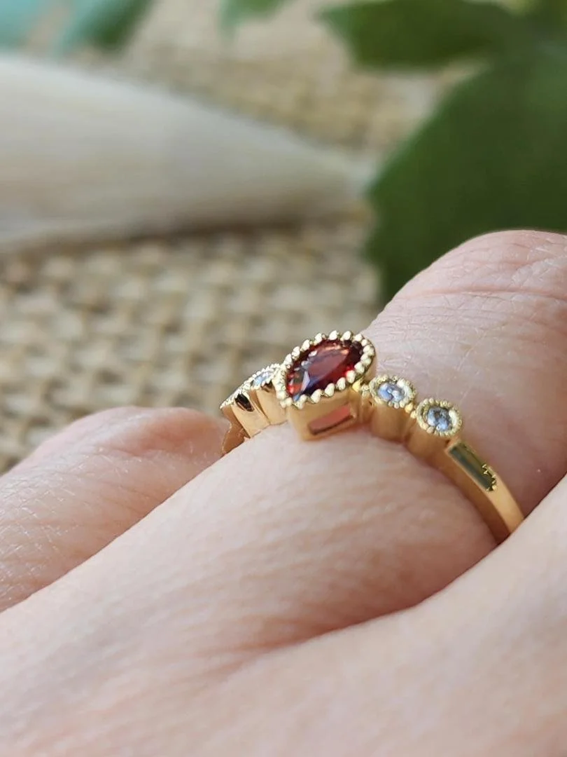 Pear shaped garnet ring in yellow gold one hand with burlap and objects in background