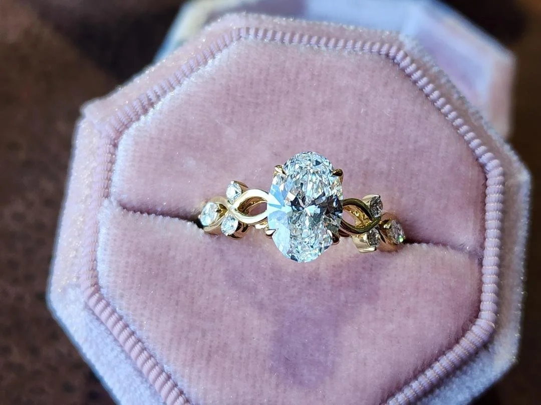 Oval lab grown diamond with rounds and marquise on the sides in yellow gold with a pink box