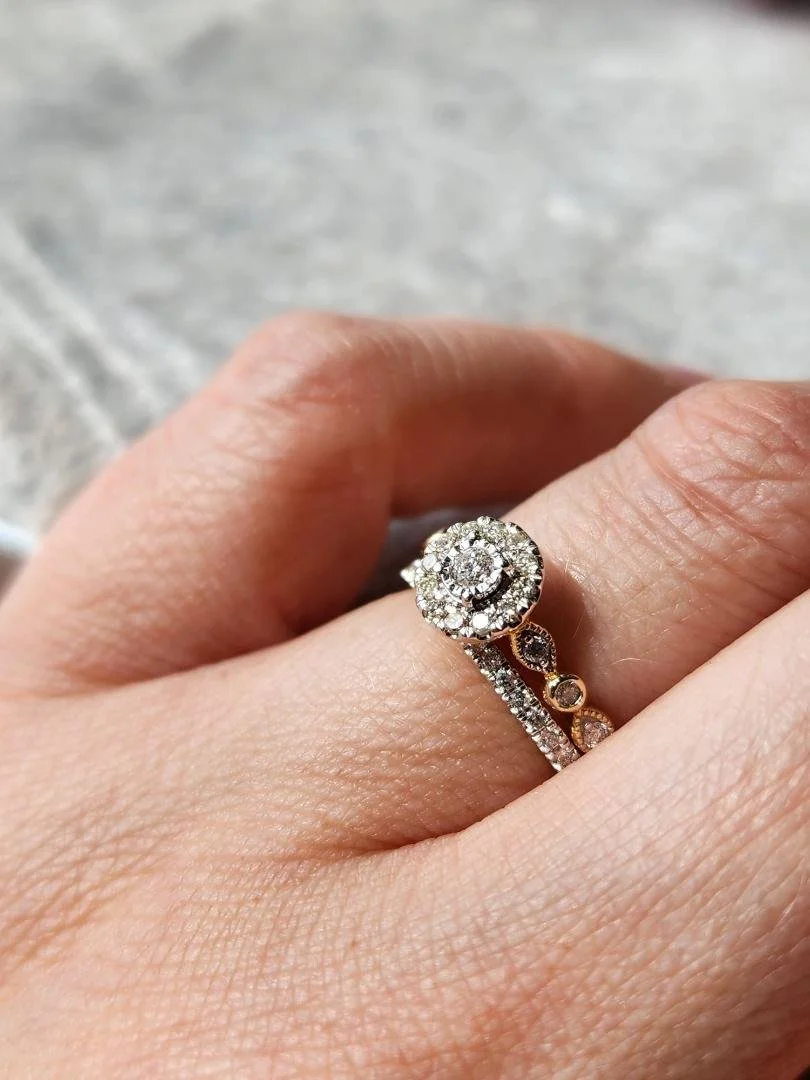One yellow gold wedding ring set with round diamond halo engagement ring and straight diamond wedding band on women's hand on grey fabric