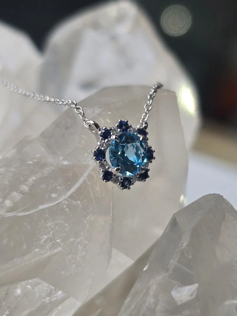 Side view of white gold blue topaz pendant with a crystal background