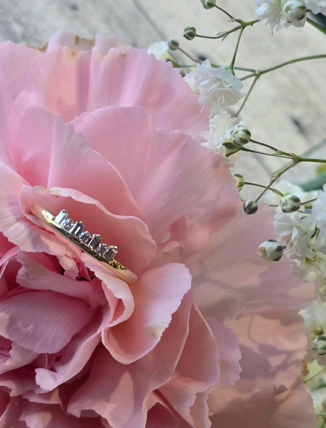 Angled view of yellow gold band set in a pink carnation with small white flower at the top