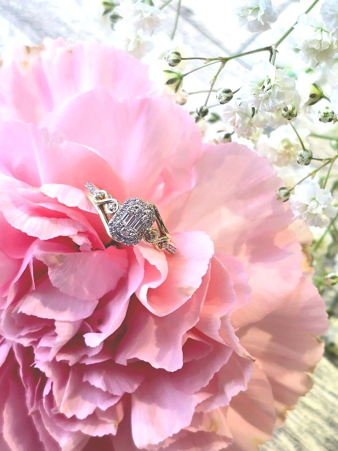 Angled view of a yellow gold engagement ring set in a pink carnation with small white flowers