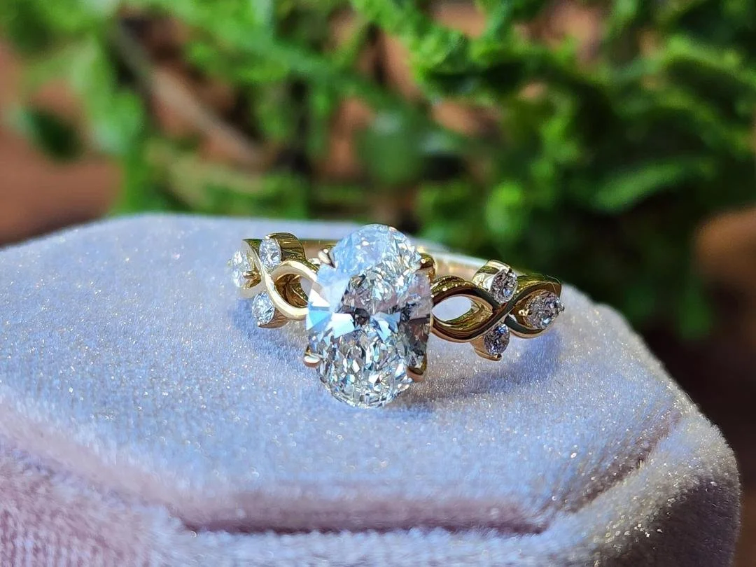 Oval lab grown diamond with rounds and marquise on the sides in yellow gold with a pink box and green in background