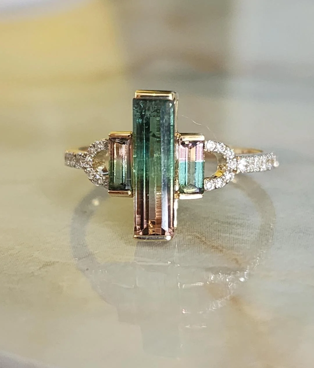 Yellow gold ring with 3 stone watermelon tourmaline and diamonds on a marble background