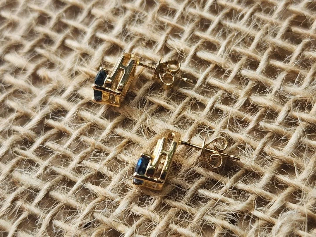 side view of One pair of yellow gold earrings featuring blue Montana sapphires with a post and friction back on a burlap background