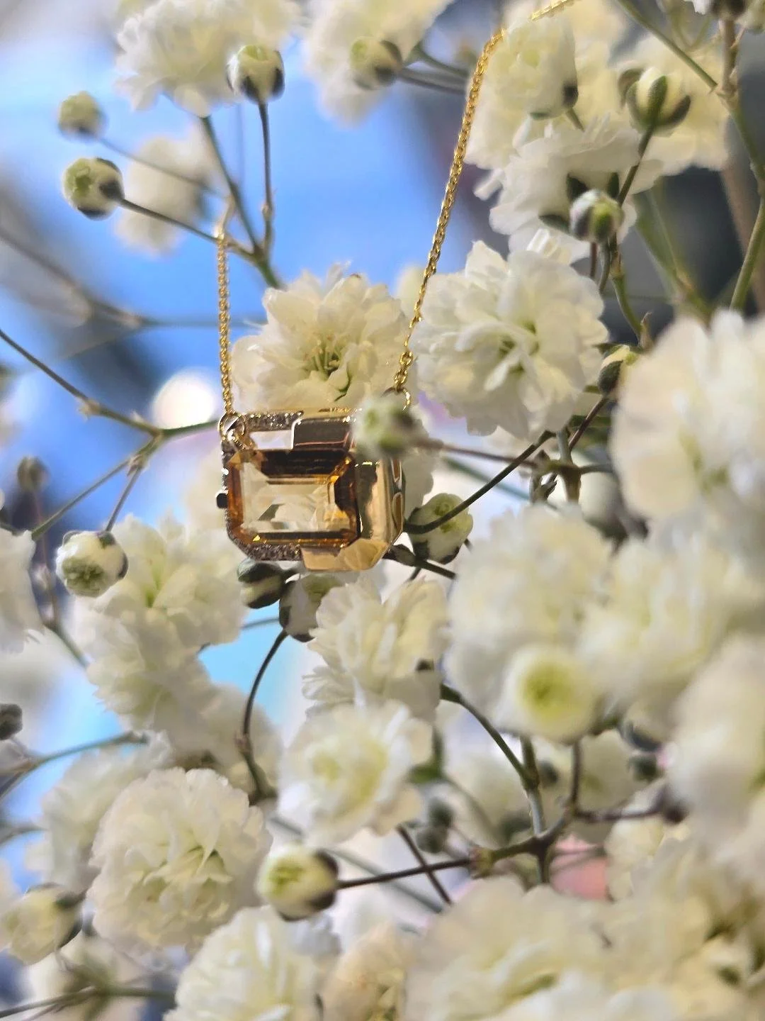 Side view of yellow gold citrine pendant on a background of small white flowers