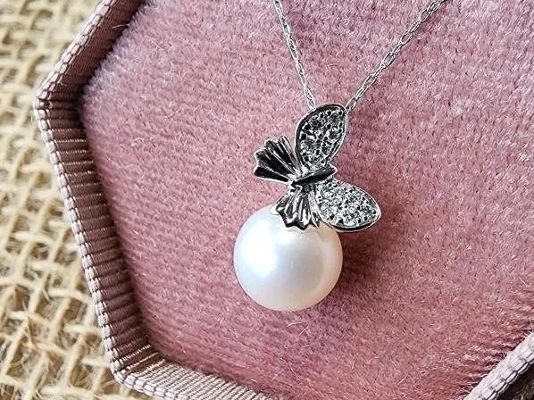 White gold diamond and pearl necklace with butterfly shape on pendant in a pink jewelry box on burlap