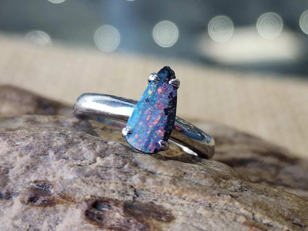 free form boulder opal set in a sterling silver ring set on a rock with burlap in the background.