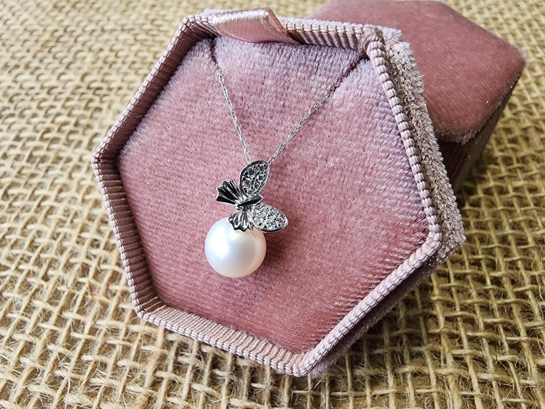 White gold diamond and pearl necklace with butterfly shape on pendant in a pink jewelry box on burlap