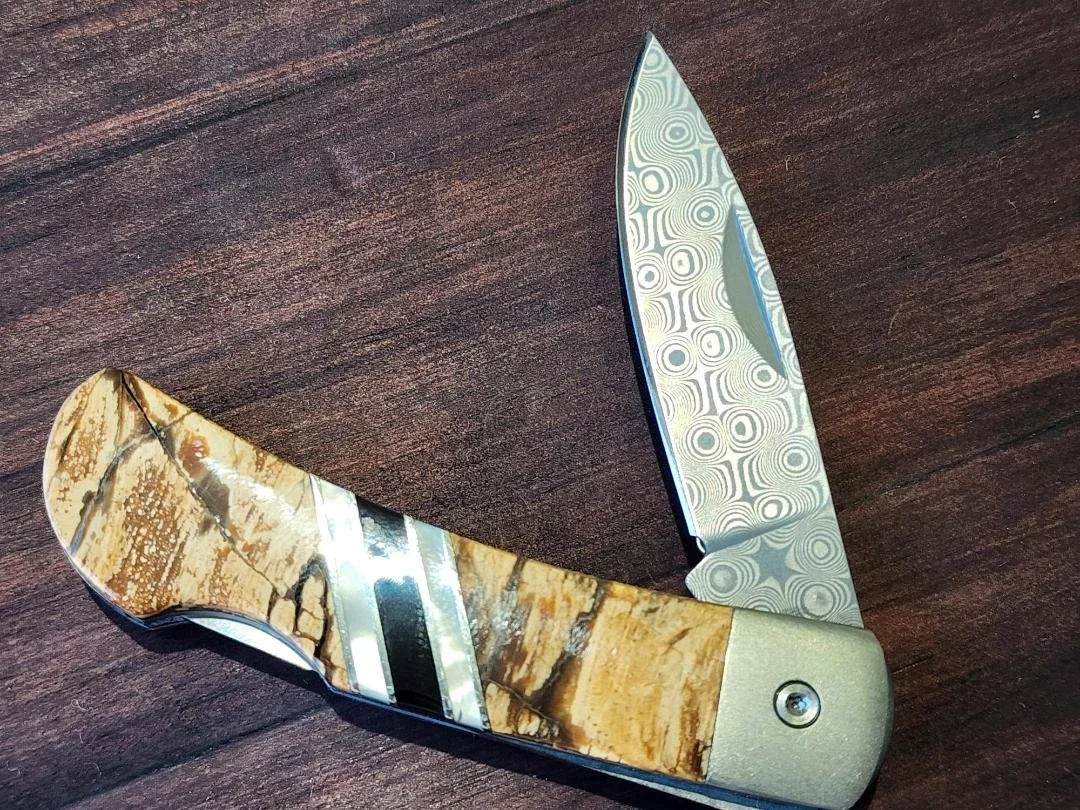 open Damascus folding pocketknife with mammoth handle and raindrop Damascus blade with wooden background