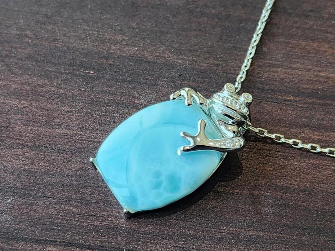 side view of blue Larimar with a necklace with frog on chain on dark wood background