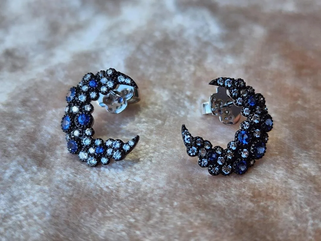 one pair of earrings with black rhodium and blue sapphire and diamonds in crescent moon on velvet fabric