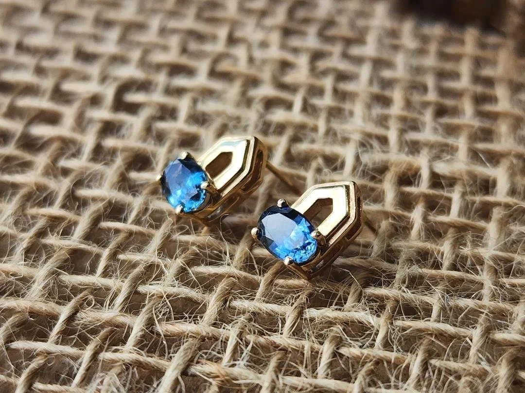 side view of One pair of yellow gold earrings featuring blue Montana sapphires on a burlap background