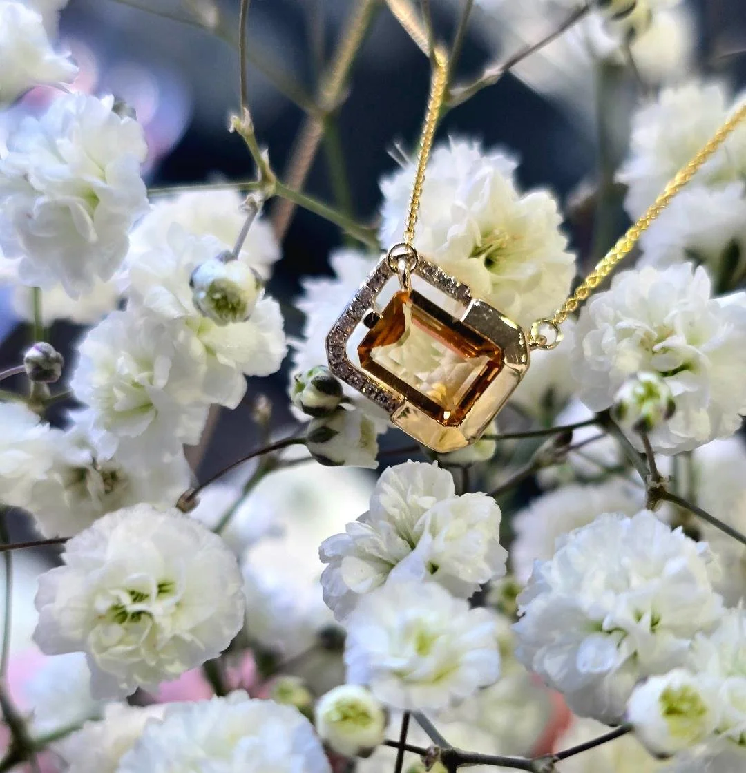 Angled view of yellow gold citrine pendant on a background of small white flowers