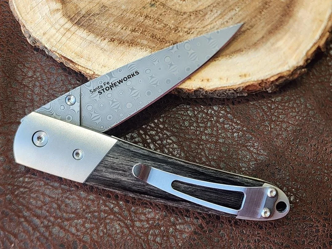 one 4" half open knife with raindrop damascus and stabilized eastern birch inlay on a wood slice and imitation leather background