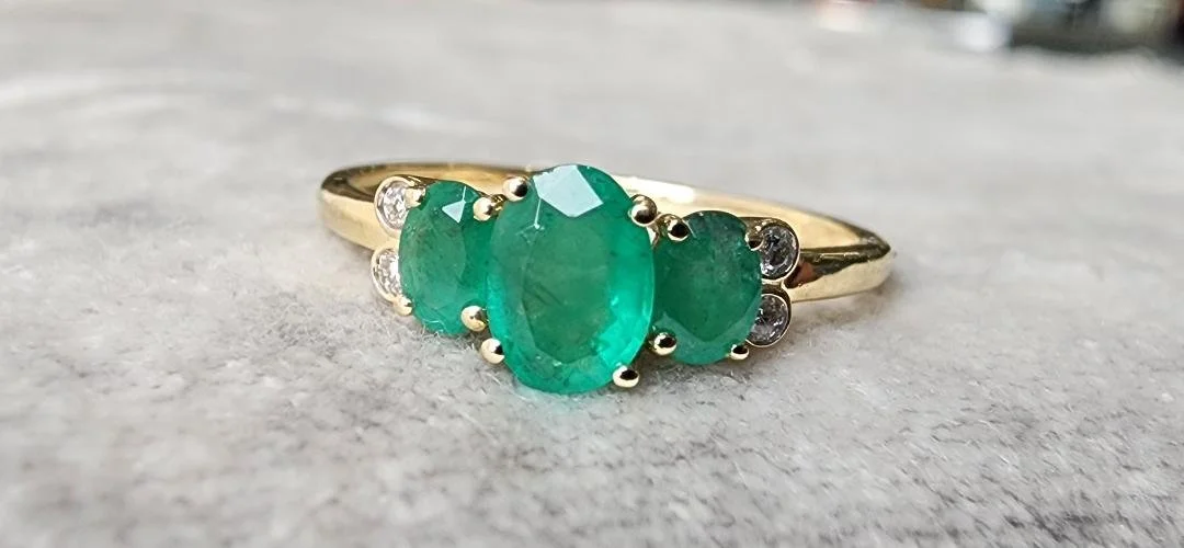 Yellow Gold 3 stone emerald ring with diamond accents on grey fabric